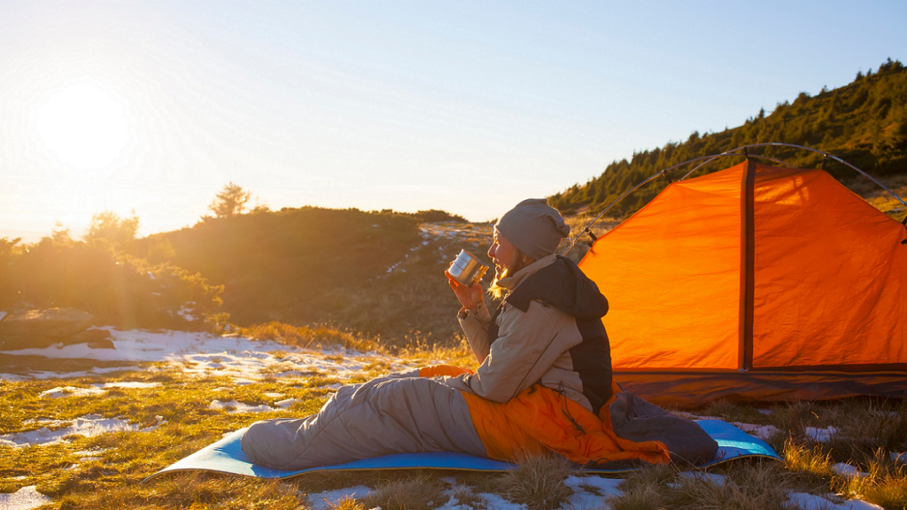 solo hiking oleh seorang perempuan yang sedang duduk menikmati sunrise dari sleeping bag